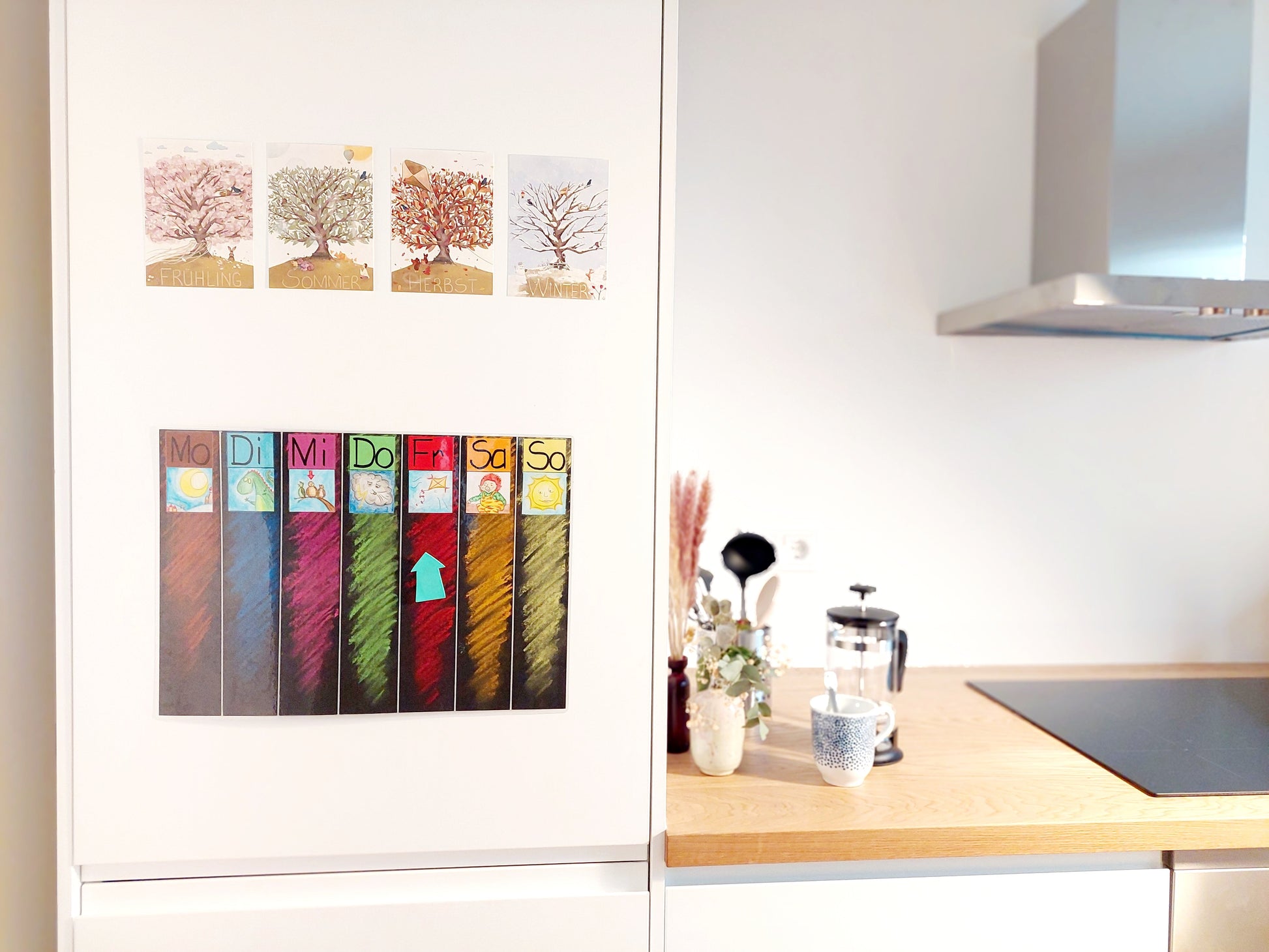 Eine helle, gemütliche Küche - Die Lernkarten hängen über einem Wochenplan für Kinder am Kühlschrank.