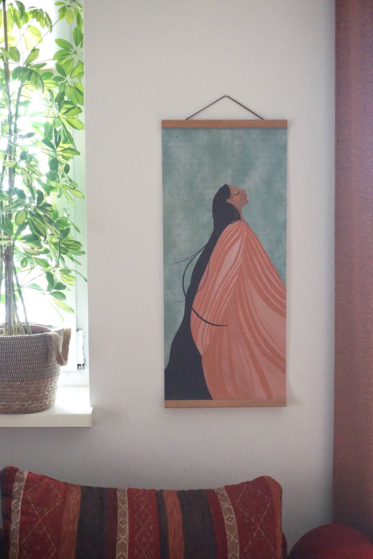 Längliches Poster Format 70cm x 30cm. Hängt mit Posterleisten im Wohnzimmer an der Wand über einer rot gemusterten gemütlichen Couch. Helles Licht scheint durch ein Fenster mit grüner Zimmerpflanze davor.