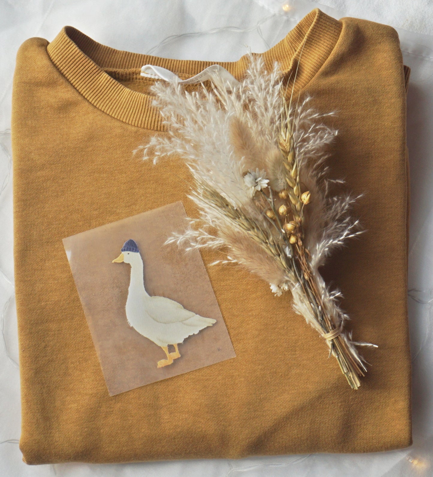 Bügelpatch von Gans mit Mütze liegt auf einem senfgelben Pullover, Seemannsgans miritime Zeichnung