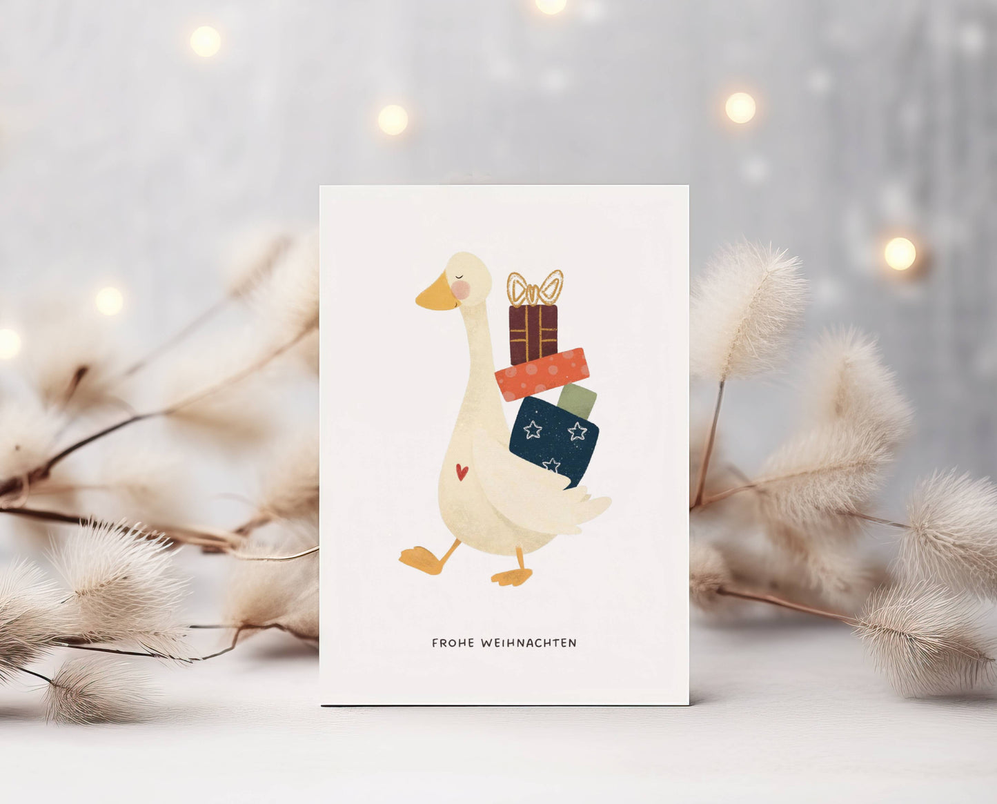 Grüße und Wünsche zu Weihnachten auf dieser süßen selbstgemalten Karte. Aquarell-Kreide-Zeichnung. Lieb lächelnde Gans mit kleinem roten Herz auf der Brust trägt stolz einen Haufen niedlicher Geschenke auf dem Rücken. Spruch: Frohe Weihnachten