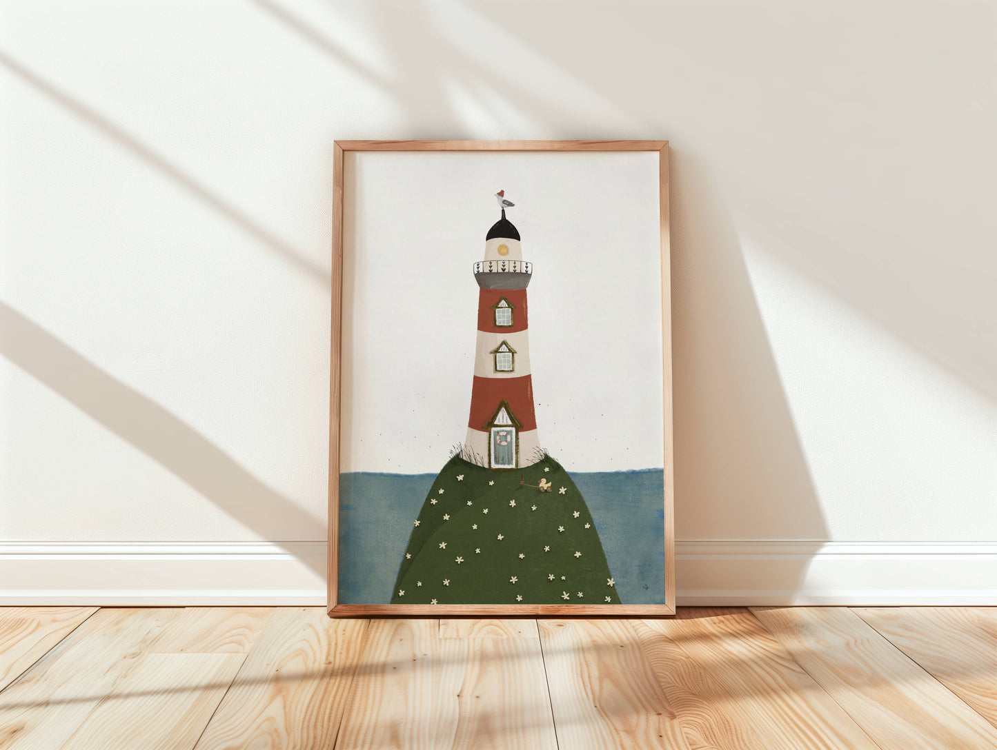 Das maritime Bild vom Leuchtturm steht eingerahmt auf einem Holzboden in einem lichtdurchflutetem Raum.