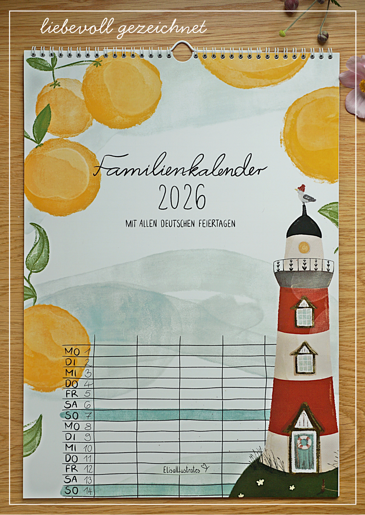Familienkalender 2026 liegt mit Blumen auf einem Holztisch. Mit handgezeichneten Aquarell-Kreide-Motiven, fünf Spalten und allen gesetzlichen Feiertagen in Deutschland. Auf dem Deckblatt ist ein Leuchtturm umringt von großen Orangen zu sehen.
