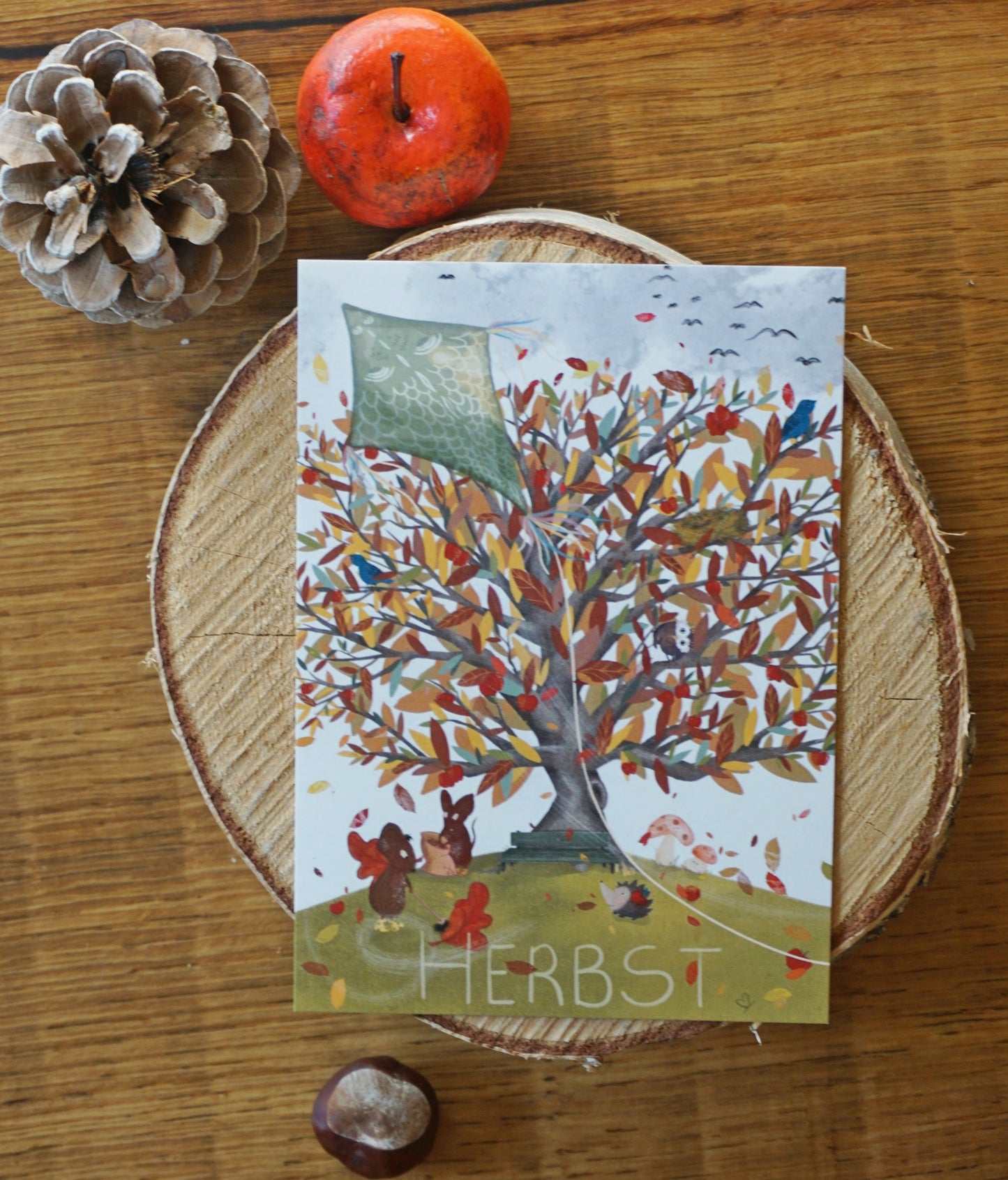 Bild Herbst Baum mit bunten Blättern, ein Drache fliegt durch die Luft, Mäuse fegen Laubblätter, ein Igel freut sich auf einen heruntergefallen Apfel, das Vogelnest ist leer.